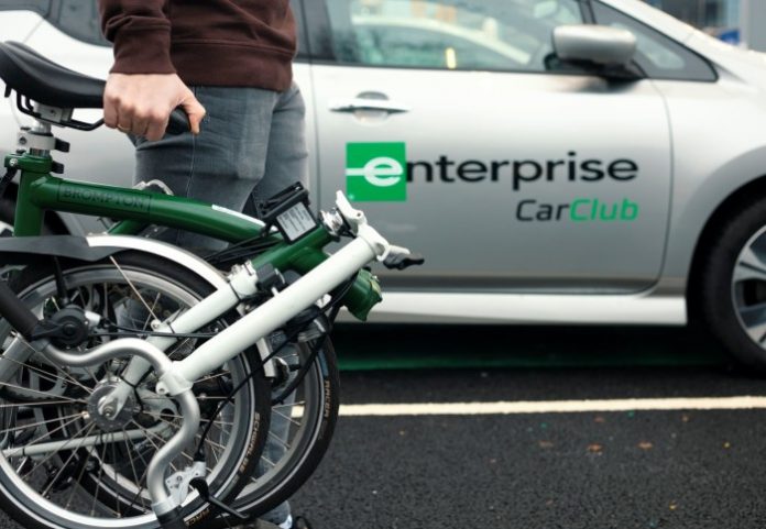 Person carrying a folding bike with a car in the background