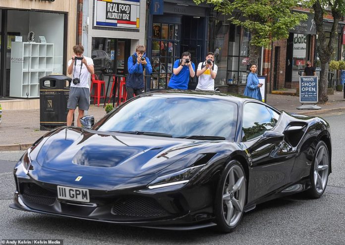 Supercar lovers try to get a picture of a glamorous black Ferrari before driving through Alderley Edge