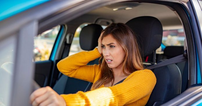Nervous female driver sits at wheel, has worried expression